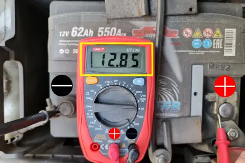Jak sprawdzić akumulator miernikiem? Wynik 12.85V wskazuje na dobry stan baterii. Czerwona sonda na plusie, czarna na minusie.