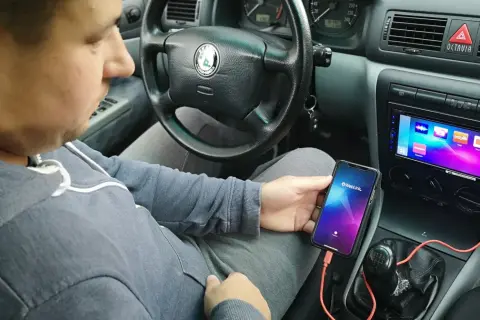 Mężczyzna w samochodzie pokazuje, jak połączyć telefon z autem za pomocą kabla i aplikacji Weblink.