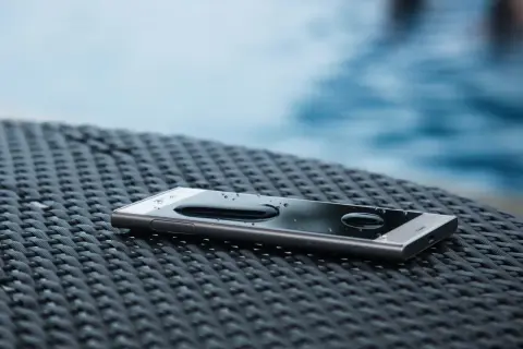 Smartfon z kroplami wody na ekranie, leżący na plecionej powierzchni. IP68 co oznacza? Ochronę przed zanurzeniem w wodzie.