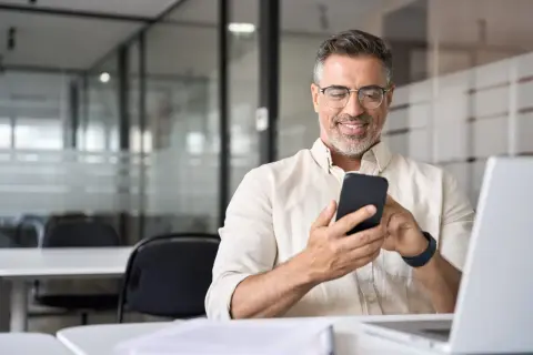 Uśmiechnięty mężczyzna z telefonem w dłoni, szukający informacji, jak udostępnić internet z telefonu na laptopa.