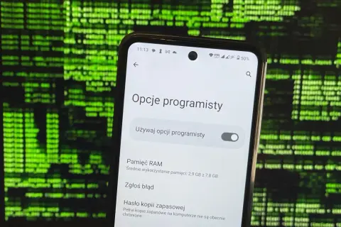 Telefon z włączonymi opcjami programisty na tle zielonego kodu.