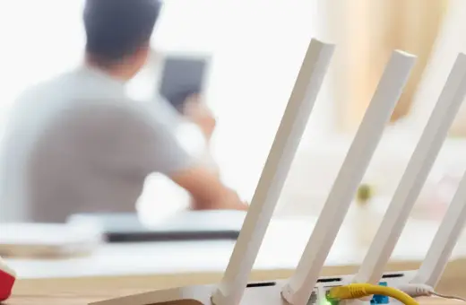 Konfiguracja routera Wi-Fi z widocznym żółtym kablem Ethernet. W tle osoba korzystająca z tabletu.