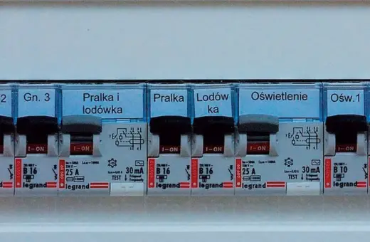 Panel z wyłącznikami i etykietami: "Pralka i lodówka", "Lodówka", "Oświetlenie". Widoczne są różne **elementy elektroniczne** i zabezpieczenia.