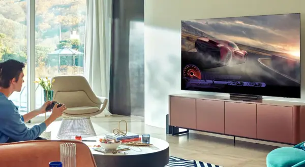 Młody mężczyzna gra w wyścigi na telewizorze 65 cali. Idealna odległość od telewizora 65 cali zapewnia immersję w grze.