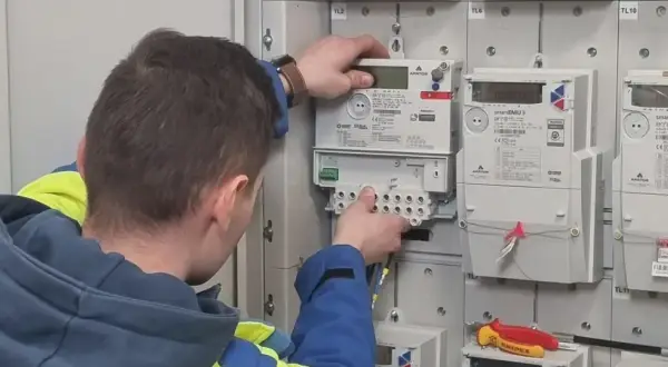 Technik w kamizelce wykonuje wymianę licznika Tauron. Widać nowe liczniki i narzędzia.