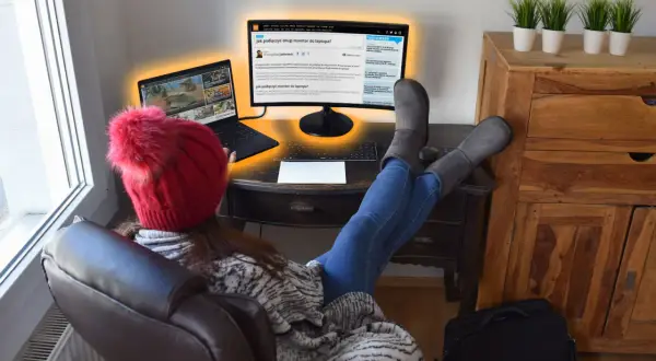 Osoba w czerwonej czapce z pomponem uczy się, jak podłączyć dwa monitory do laptopa, korzystając z artykułu na ekranie.