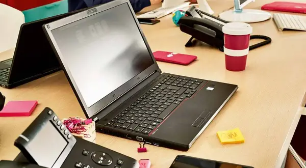 Biurko z laptopem, telefonem i kubkiem. Dowiedz się, jak połączyć telefon z laptopem, aby praca była efektywniejsza.
