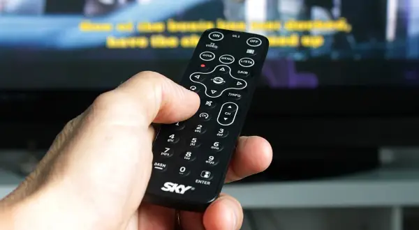 Dłoń trzyma pilot, by jak wyszukać kanały w telewizorze. Widoczne przyciski MENU, LISTA i CH.