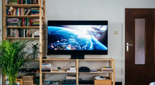 Nowoczesny salon z telewizorem o wymiarach 43 cale, wyświetlającym Ziemię z kosmosu. Obok regał z książkami i roślinami.
