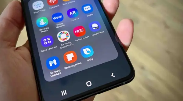 Na ekranie telefonu widać ikony aplikacji, w tym Bixby, Samsung Health, Galaxy Wearable i Game Launcher.