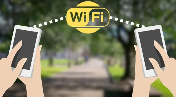 Dwie dłonie trzymają telefony, między którymi widoczny jest symbol Wi-Fi. Połączenie wifi direct umożliwia szybką wymianę danych.