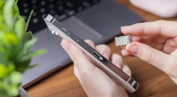 Ręka trzyma duplikat karty SIM obok telefonu.