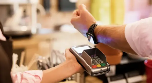 Klient płaci zbliżeniowo zegarkiem z technologią nfc przy terminalu płatniczym.