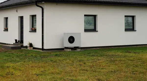Nowoczesna pompa ciepła przy białym domu. Idealna do ogrzania domu 150m2, zapewnia komfort i oszczędność.