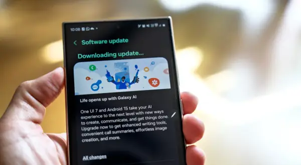 Dłoń trzyma smartfon z ekranem aktualizacji oprogramowania "Downloading update..." z grafiką Galaxy AI.