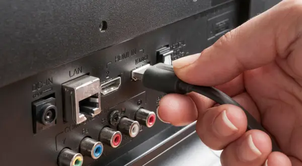 Dłoń podłącza kabel do portu HDMI ARC w telewizorze. Dowiedz się, hdmi arc co to za funkcja.
