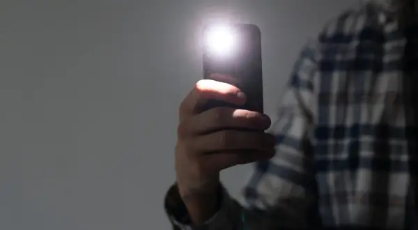 Dłoń trzyma smartfon z włączoną latarką. Dowiedz się, jak wyłączyć latarkę w telefonie, aby oszczędzać baterię.