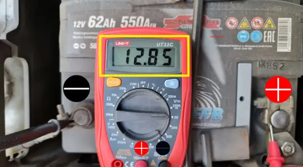Jak sprawdzić akumulator miernikiem? Wynik 12.85V wskazuje na dobry stan baterii. Czerwona sonda na plusie, czarna na minusie.