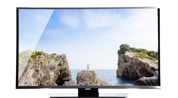 Na ekranie telewizora widok na morze, skały i osobę z rękami w górze. Brak obrazu w telewizorze, gdyby nie ten piękny krajobraz.