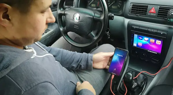 Mężczyzna w samochodzie pokazuje, jak połączyć telefon z autem za pomocą kabla i aplikacji Weblink.