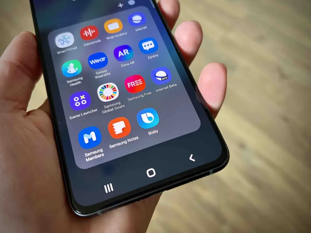 Na ekranie telefonu widać ikony aplikacji, w tym Bixby, Samsung Health, Galaxy Wearable i Game Launcher.
