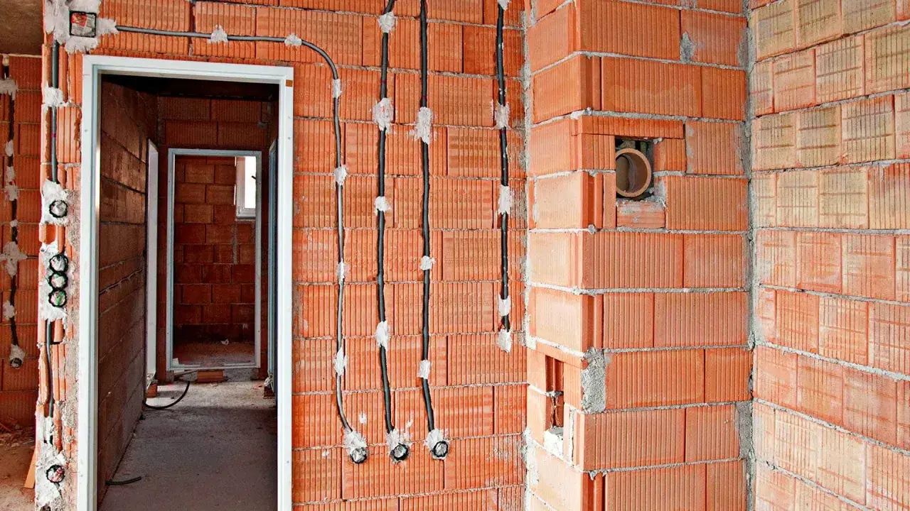 Instalacja elektryczna bezpuszkowa w budowie. Widoczne przewody i puszki instalacyjne w ścianach z cegły.