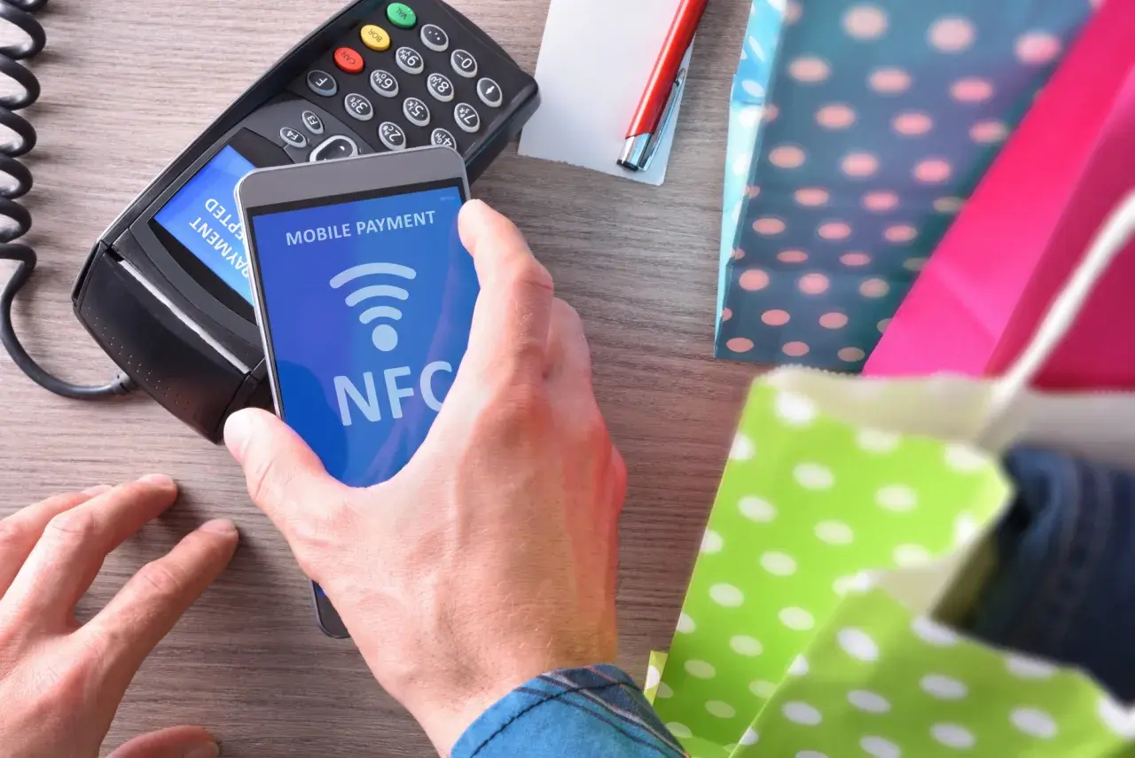 Płatność zbliżeniowa telefonem z funkcją NFC. Transakcja w toku, obok kolorowe torby na zakupy.