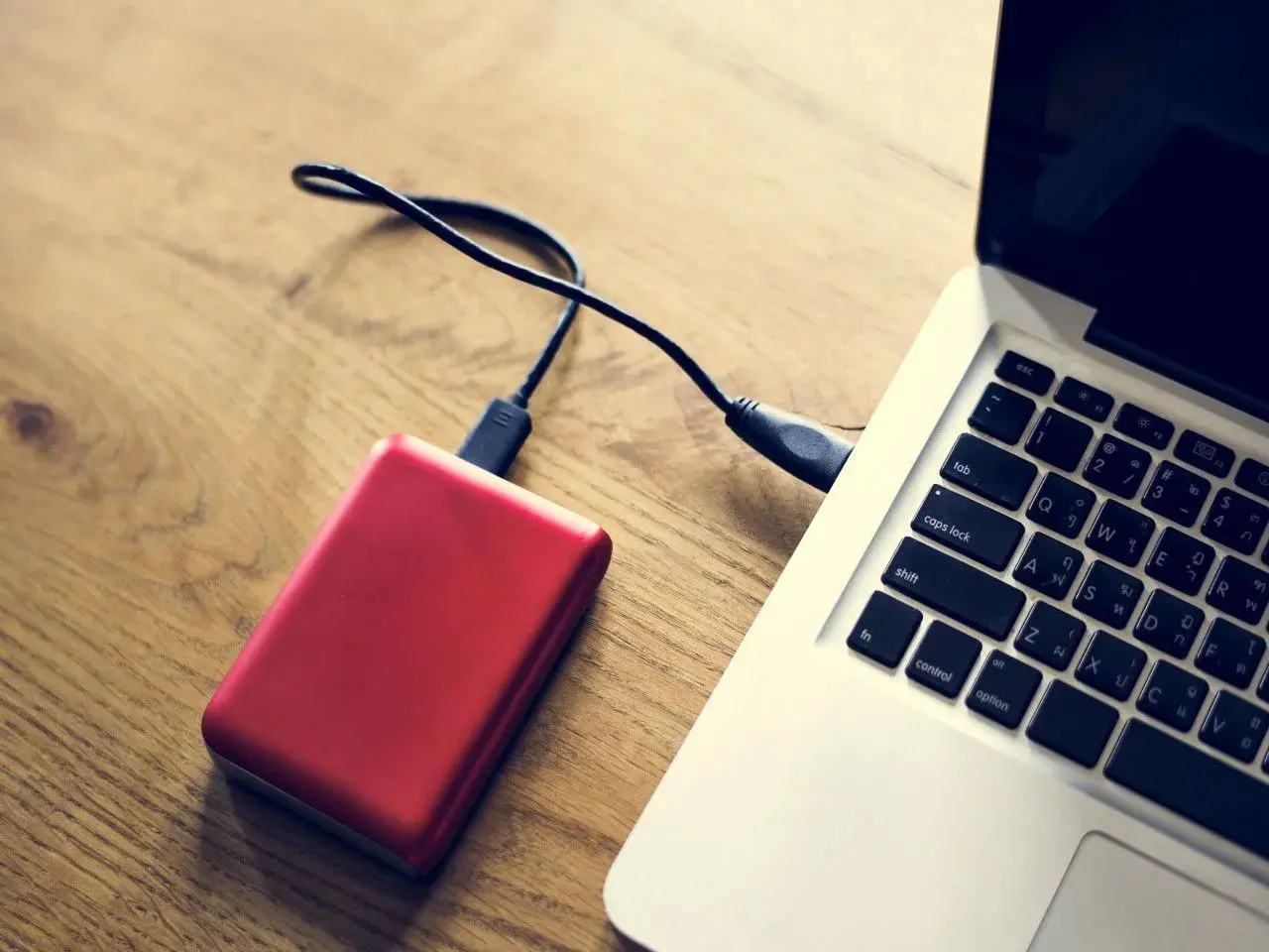Czerwony dysk zewnętrzny podłączony do laptopa. Komputer nie widzi dysku zewnętrznego, co może być frustrujące.