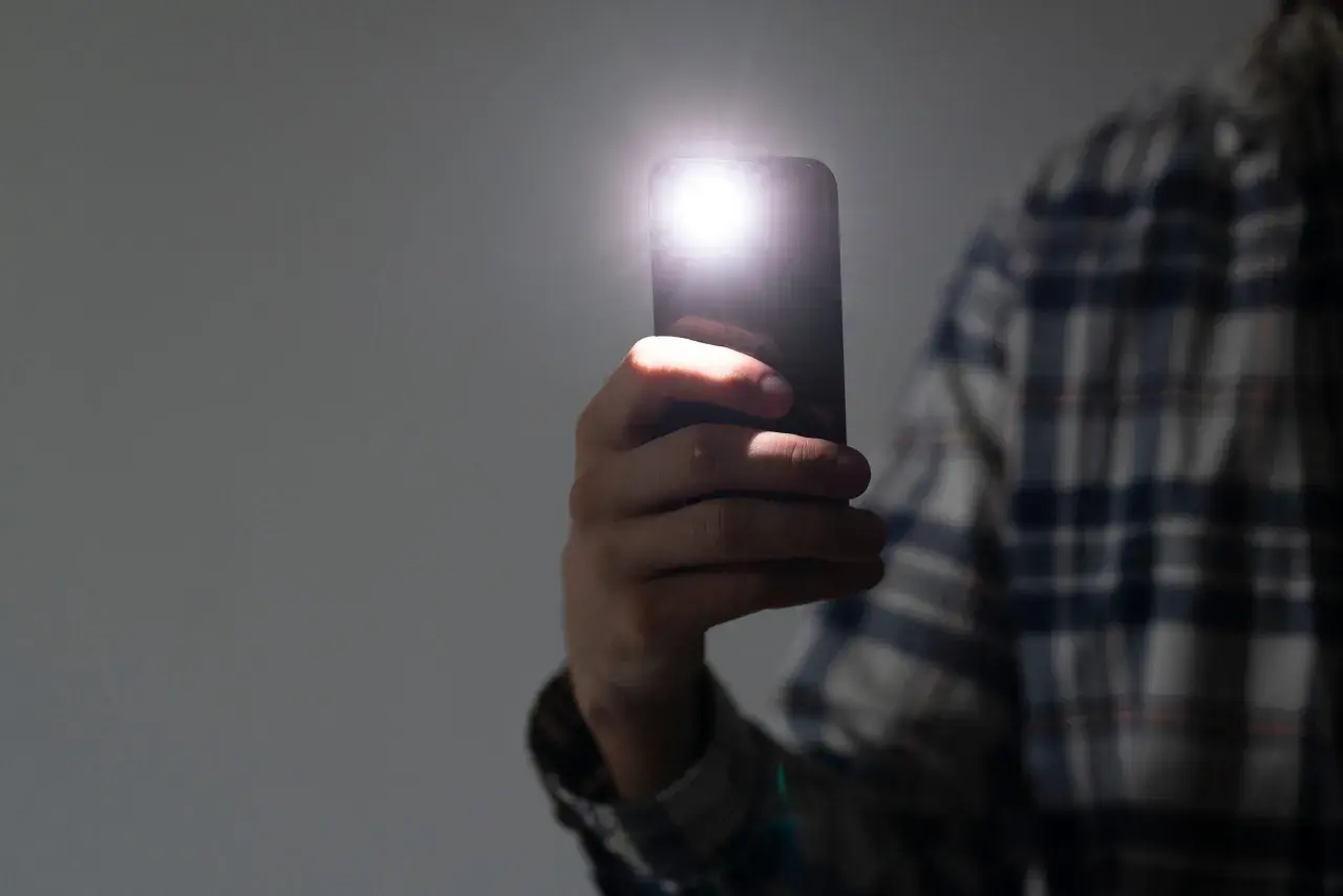 Dłoń trzyma smartfon z włączoną latarką. Dowiedz się, jak wyłączyć latarkę w telefonie, aby oszczędzać baterię.