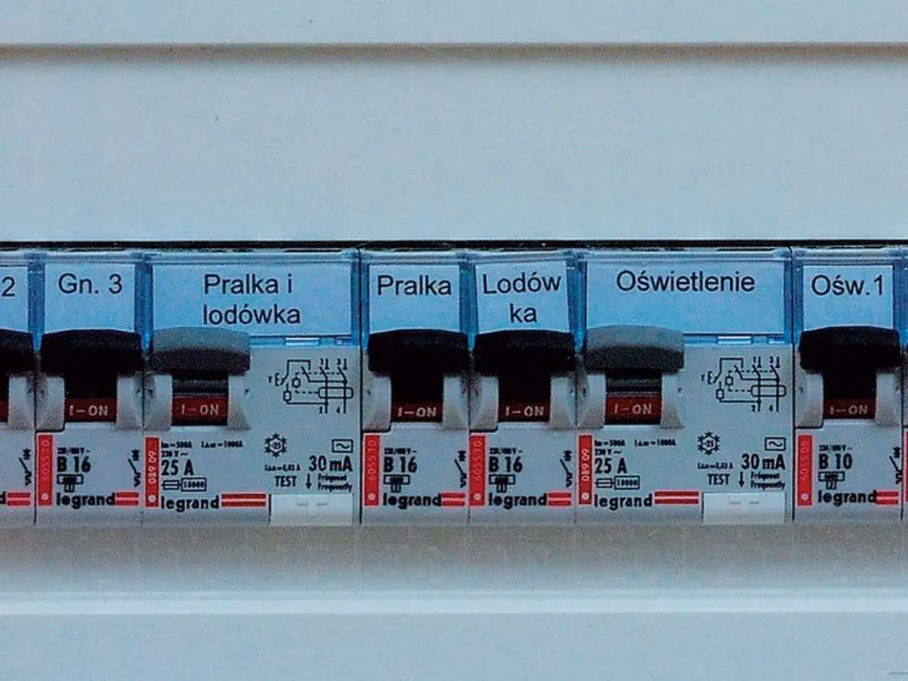 Panel z wyłącznikami i etykietami: "Pralka i lodówka", "Lodówka", "Oświetlenie". Widoczne są różne **elementy elektroniczne** i zabezpieczenia.