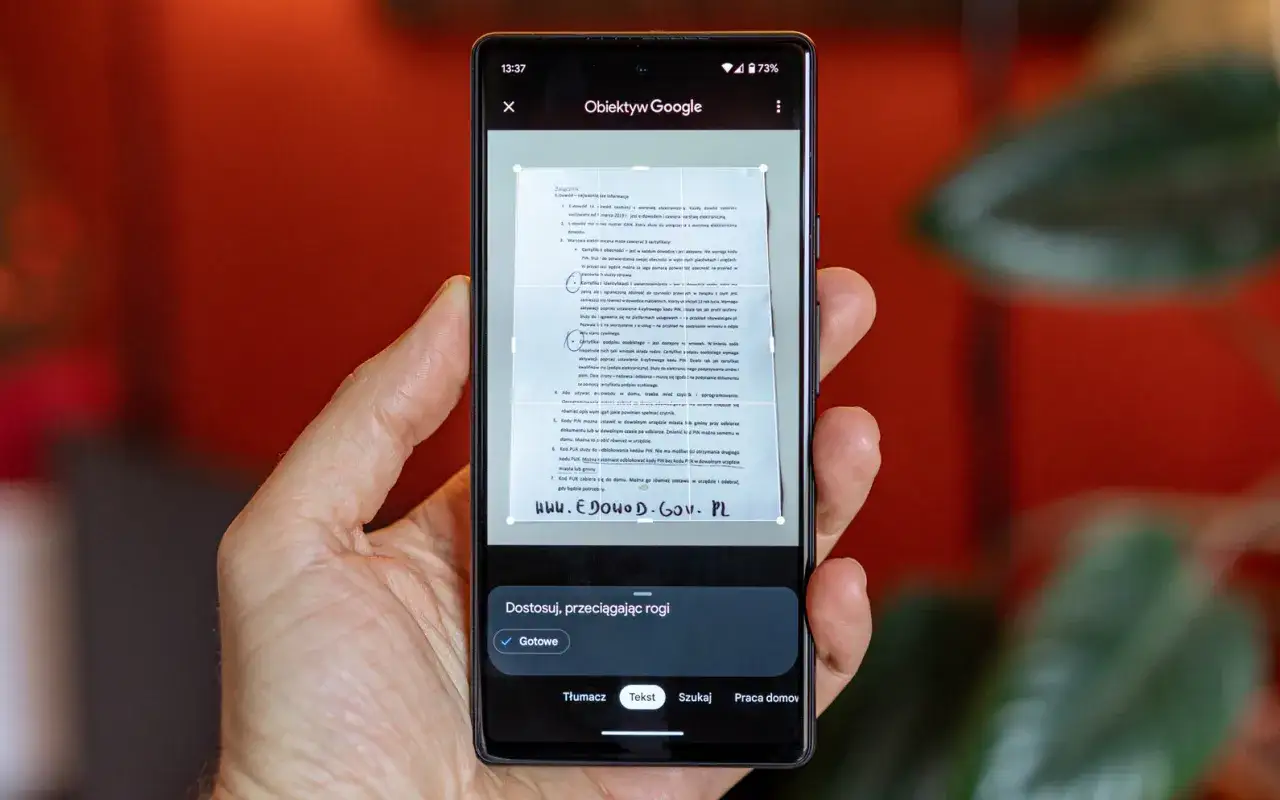 Ręka trzyma smartfon, na ekranie którego działa skaner w telefonie, skanując dokument.