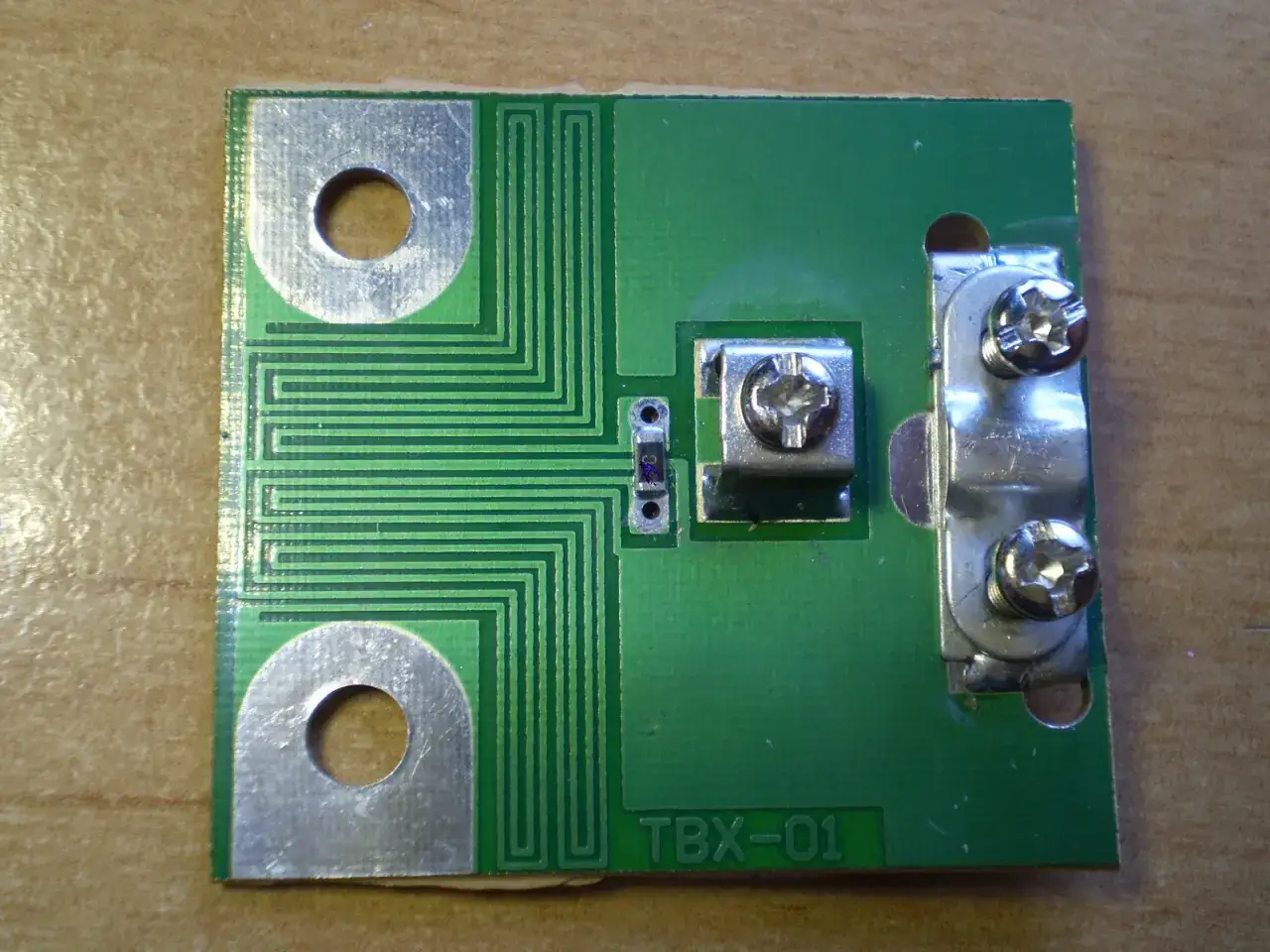Zielony symetryzator TBX-01 z metalowymi złączami i śrubami, gotowy do montażu.