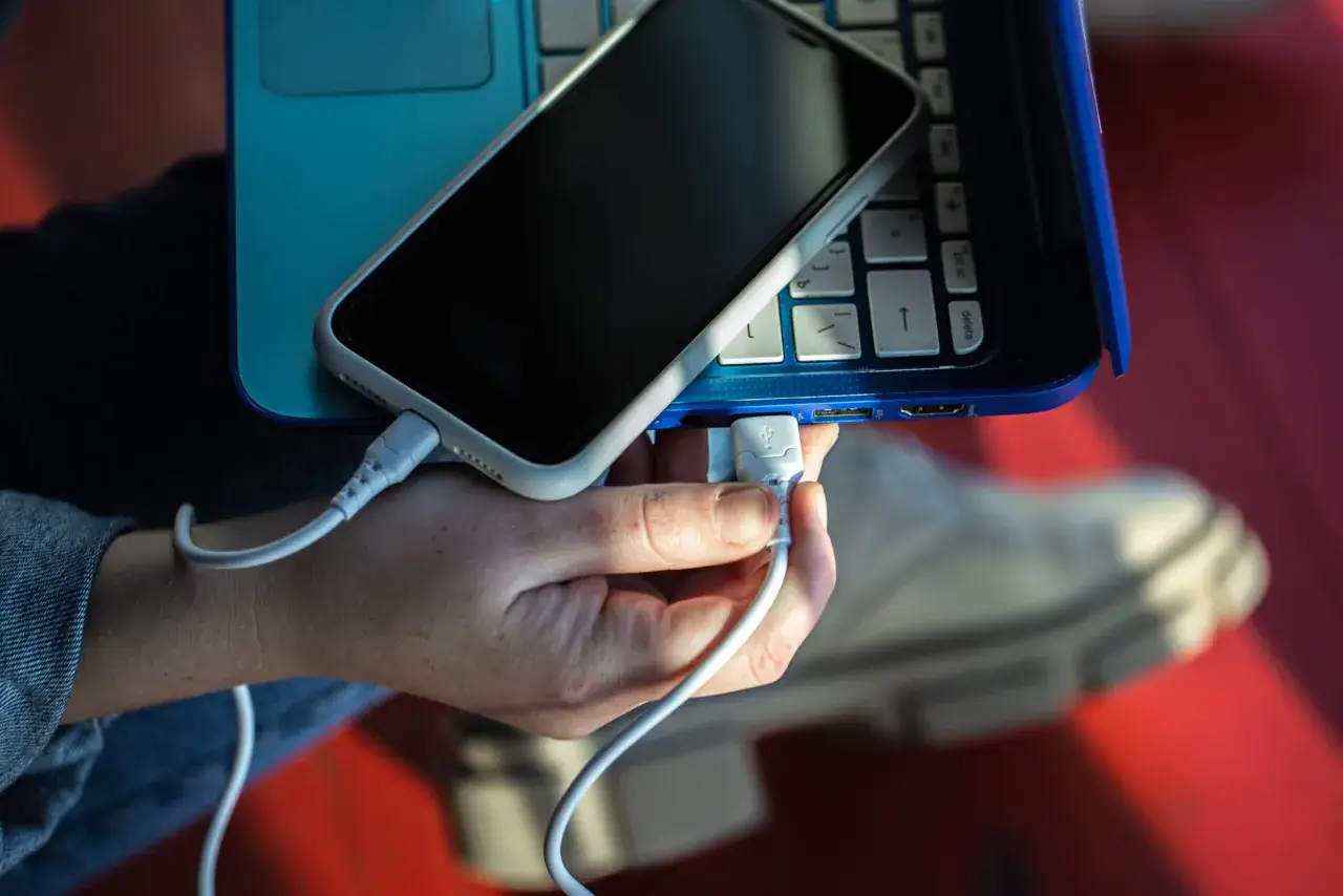 Ręka podłącza telefon do laptopa za pomocą kabla USB. Prosty sposób, jak połączyć telefon z laptopem, by przesłać dane lub naładować urządzenie.
