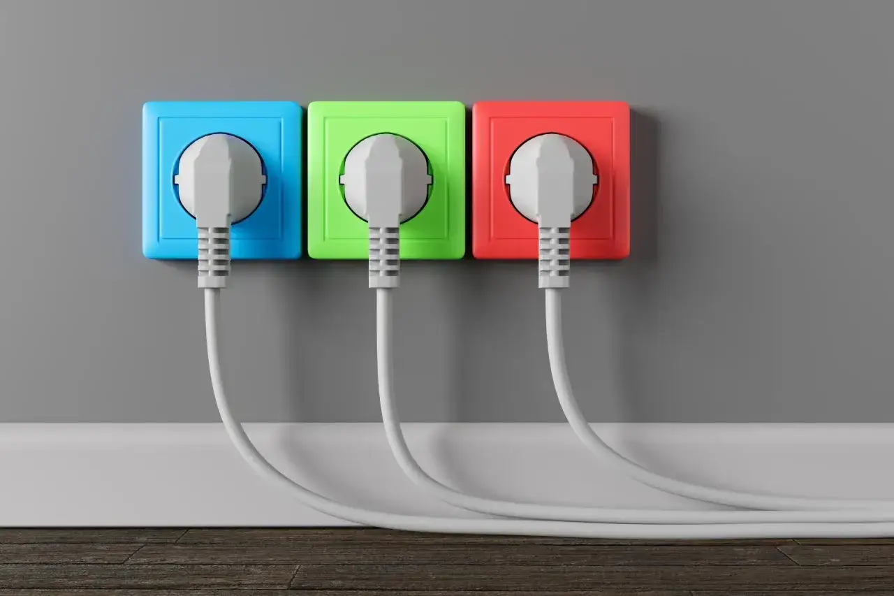 Kolorowe gniazdka elektryczne (niebieskie, zielone, czerwone) z wtyczkami, tworzące nowoczesną instalację elektryczną bezpuszkową.