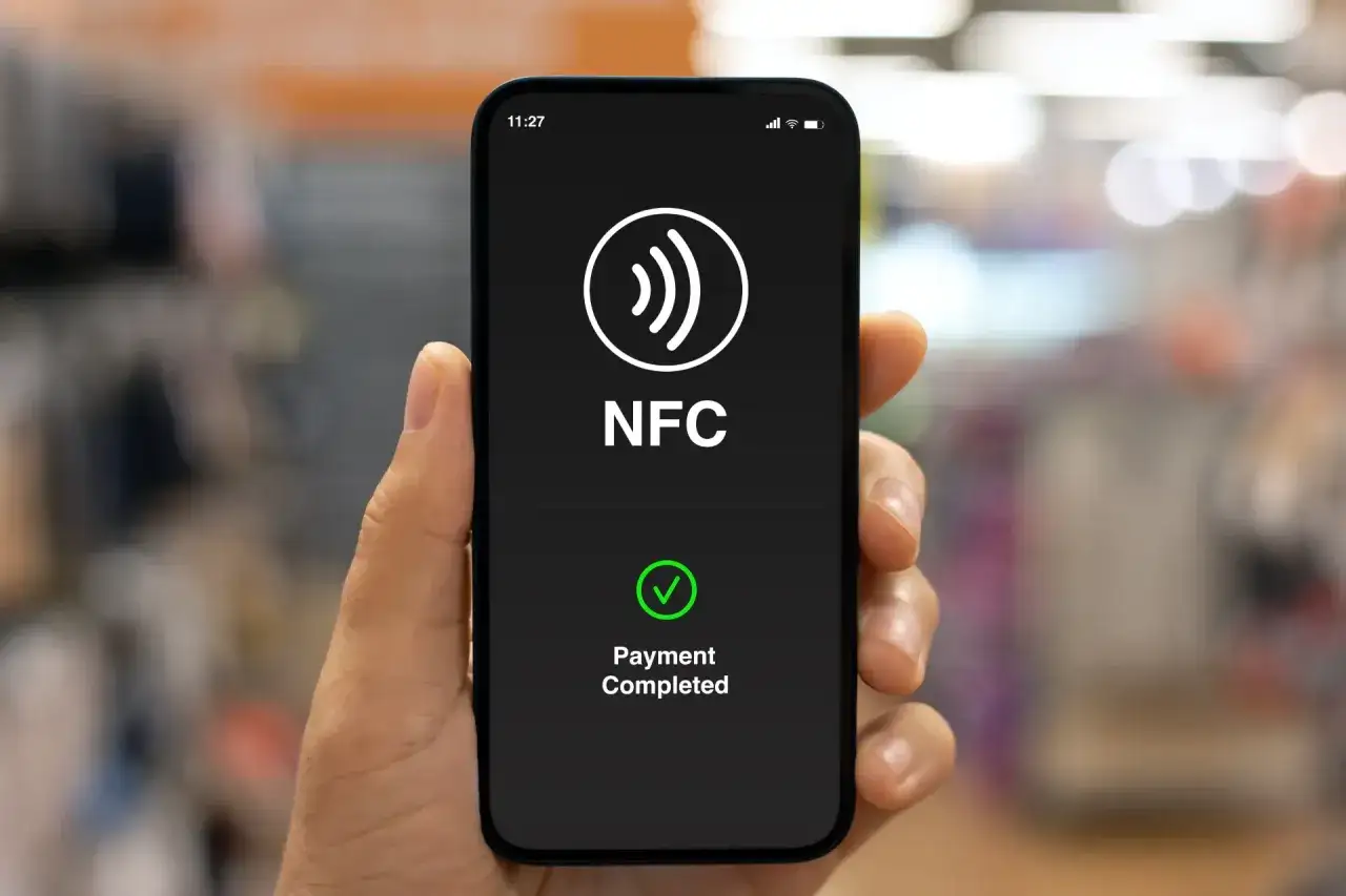Dłoń trzyma smartfon z ekranem pokazującym symbol NFC i komunikat 