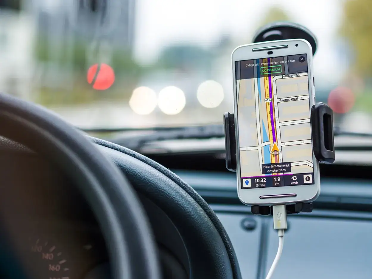 Telefon w uchwycie na desce rozdzielczej, z nawigacją GPS. Pokazuje, jak połączyć telefon z samochodem, by wygodnie podróżować.