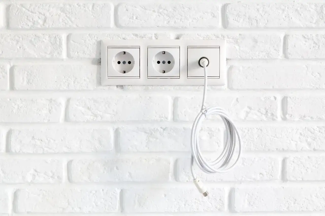 Nowoczesna instalacja elektryczna bezpuszkowa z trzema gniazdkami na białej ceglanej ścianie. Jeden kabel zwisa swobodnie.