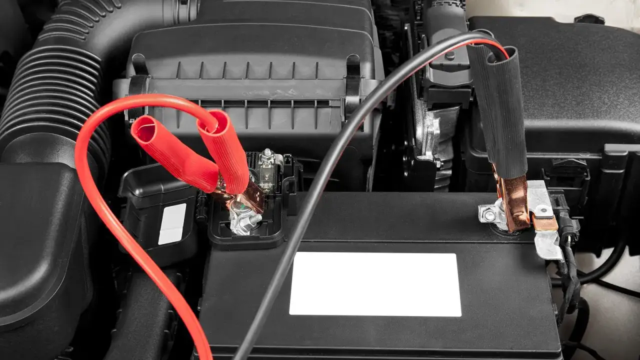 Czerwone kable rozruchowe podłączone do akumulatora samochodowego. Pokazano, jak podłączyć kable do akumulatora, aby uruchomić auto.