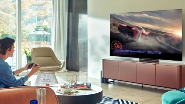 Młody mężczyzna gra w wyścigi na telewizorze 65 cali. Idealna odległość od telewizora 65 cali zapewnia immersję w grze.
