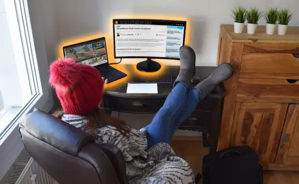 Osoba w czerwonej czapce z pomponem uczy się, jak podłączyć dwa monitory do laptopa, korzystając z artykułu na ekranie.