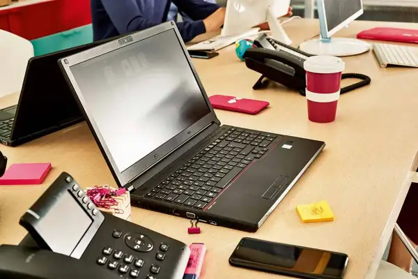 Biurko z laptopem, telefonem i kubkiem. Dowiedz się, jak połączyć telefon z laptopem, aby praca była efektywniejsza.