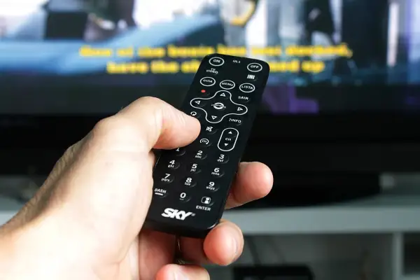 Dłoń trzyma pilot, by jak wyszukać kanały w telewizorze. Widoczne przyciski MENU, LISTA i CH.