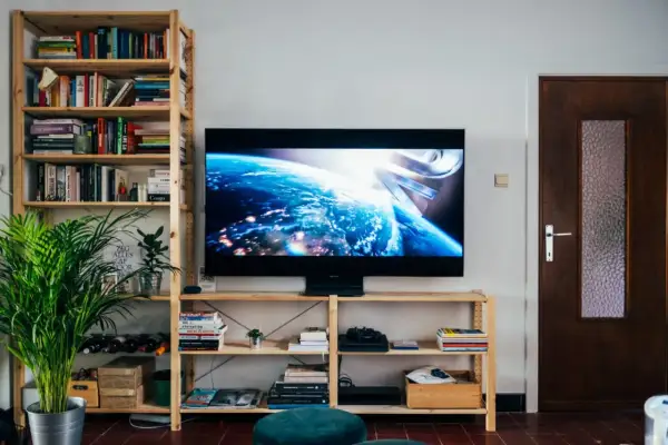 Nowoczesny salon z telewizorem o wymiarach 43 cale, wyświetlającym Ziemię z kosmosu. Obok regał z książkami i roślinami.
