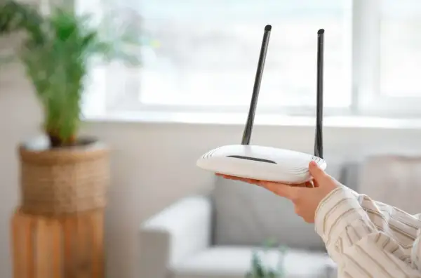 Dłoń trzyma biały router z dwiema antenkami. Może to być pierwszy krok, jak zresetować router, gdy internet przestaje działać.