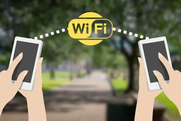 Dwie dłonie trzymają telefony, między którymi widoczny jest symbol Wi-Fi. Połączenie wifi direct umożliwia szybką wymianę danych.