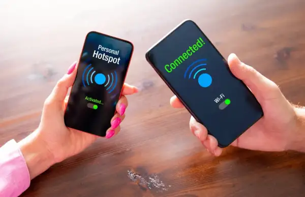 Dwie dłonie trzymają telefony. Na jednym ekranie "Personal Hotspot Activated...", na drugim "Connected! Wi-Fi".