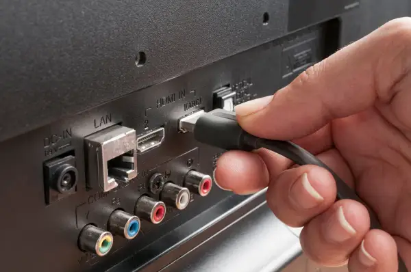 Dłoń podłącza kabel do portu HDMI ARC w telewizorze. Dowiedz się, hdmi arc co to za funkcja.