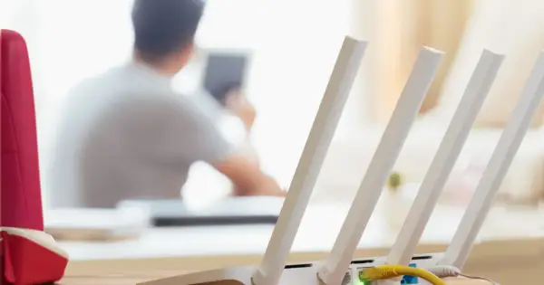 Konfiguracja routera Wi-Fi z widocznym żółtym kablem Ethernet. W tle osoba korzystająca z tabletu.