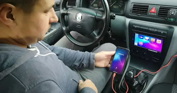 Mężczyzna w samochodzie pokazuje, jak połączyć telefon z autem za pomocą kabla i aplikacji Weblink.